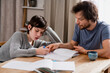 © Елена Григорович - Teenager boy doing school lessons at home. Dad helping solve difficult math problems. Problems and difficulties of home education