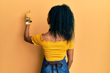 Middle age african american woman wearing professional apron posing backwards pointing ahead with finger hand