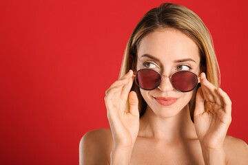 Poster - Beautiful woman in stylish sunglasses on red background. Space for text