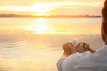 Wall Mural - Couple holding beautiful flower near river at sunset, closeup view with space for text. Nature healing power