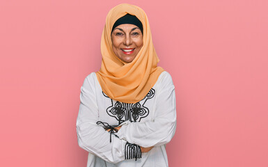 Middle age hispanic woman wearing traditional islamic hijab scarf happy face smiling with crossed arms looking at the camera. positive person.