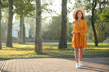 Canvas Print - Beautiful young woman wearing stylish yellow dress and straw hat in park