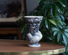 Abstract Syle Ceramic Vase - Bird Shape With Stylized Animals - On A Wooden Table, In The Background Plants