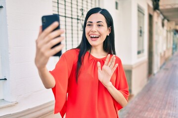 Wall Mural - Young latin girl smiling happy doing video call using smartphone at the city.