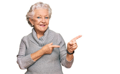 Senior grey-haired woman wearing casual winter sweater smiling and looking at the camera pointing with two hands and fingers to the side.