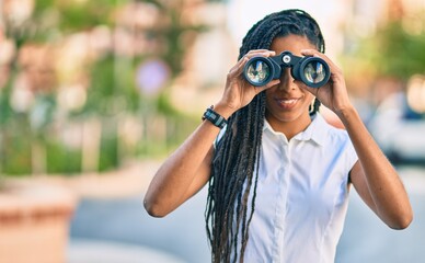 Poster - young african american woman smiling happy looking for new opportunity using binoculars at the city.