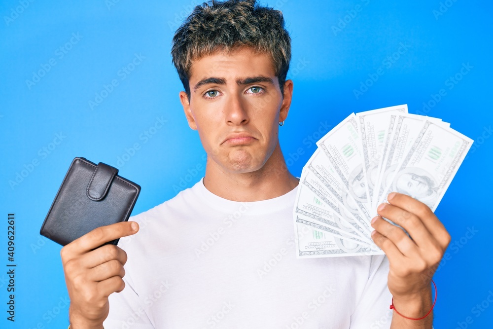 Young handsome man holding wallet and dollars banknotes depressed and worry for distress, crying angry and afraid. sad expression. - obrazy, fototapety, plakaty 