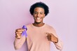 © Krakenimages.com - African american man with afro hair holding awareness purple ribbon smiling happy pointing with hand and finger