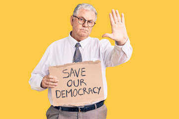 Sticker - Senior grey-haired man wearing business clothes holding save our democracy protest banner with open hand doing stop sign with serious and confident expression, defense gesture