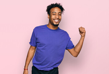 Young african american man with beard wearing casual purple t shirt smiling with happy face looking and pointing to the side with thumb up.