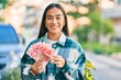 Young latin girl smiling happy counting chinese yuan banknotes at the city.