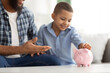 © Prostock-studio - Black Dad And Son Putting Coin In Piggybank Indoors, Cropped