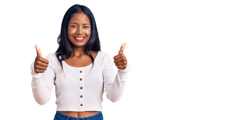 Wall Mural - Young indian girl wearing casual clothes success sign doing positive gesture with hand, thumbs up smiling and happy. cheerful expression and winner gesture.