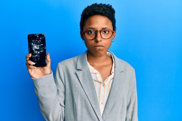 Wall Mural - Young african american girl holding broken smartphone showing cracked screen thinking attitude and sober expression looking self confident