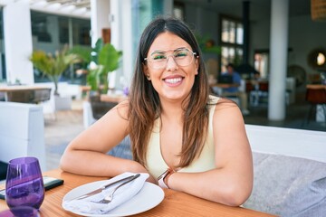 Wall Mural - Young beautiful hispanic woman smiling happy. Sitting on the table looking at the camera at restaurant