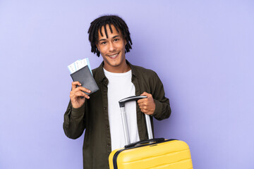 Wall Mural - Young african american man isolated on purple background in vacation with suitcase and passport