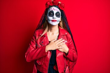 Wall Mural - Woman wearing day of the dead costume over red smiling with hands on chest with closed eyes and grateful gesture on face. health concept.