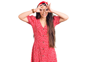 Wall Mural - Brunette teenager girl wearing summer dress doing ok gesture like binoculars sticking tongue out, eyes looking through fingers. crazy expression.