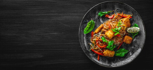 Wall Mural - Tasty asian noodles with fried cheese tofu and vegetables in plate on black wooden table background