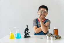 Education Scientists Concept. Little Kid Scientific Boy Holding Magnifying In His Hand Front View Eye With Microscope And Tube Experiment On The Desk While Looking At Something At Science Lab Room.