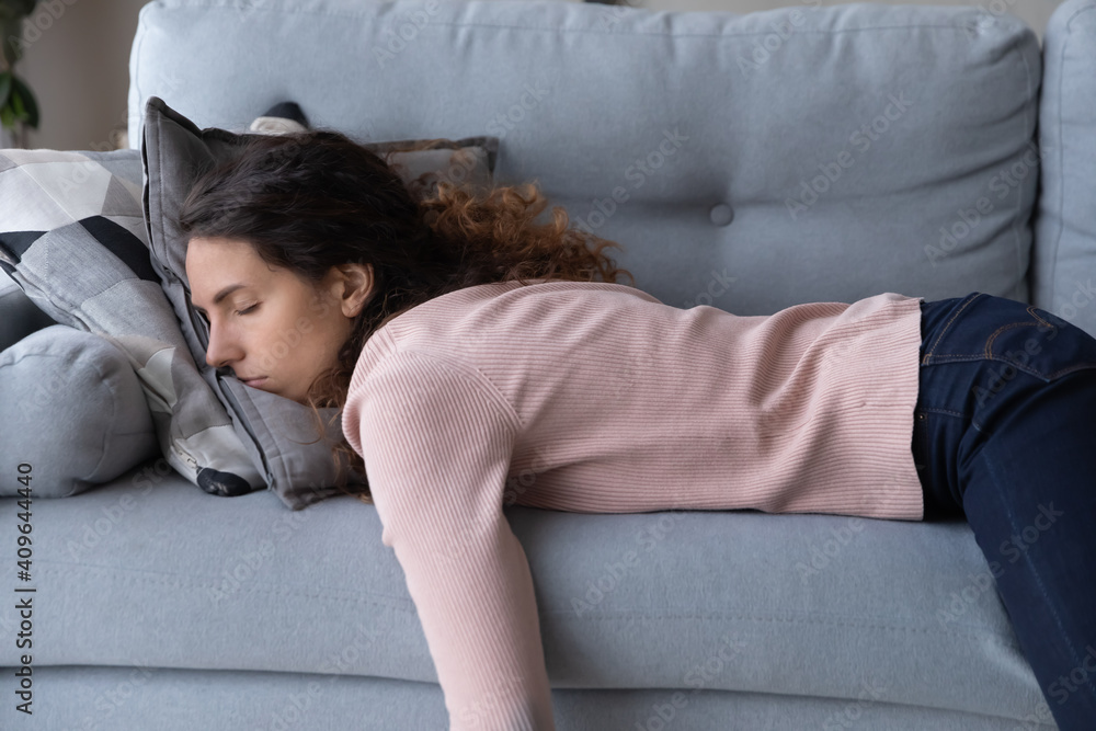 Tired unmotivated young woman falls asleep on cozy couch indoors, having no energy after hard working day. Exhausted caucasian lady napping on comfortable sofa in living room, fatigue concept.