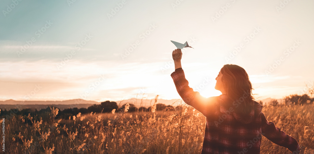 Travelling woman with paper airplane enjoying life and freedom at the land at sunset. Arms outstretched and happiness - obrazy, fototapety, plakaty 