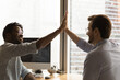 © fizkes - Give me five. Diverse colleagues black and caucasian managers employees join hands high celebrate common achievement. Two young men successful teammates friends greet each other with great job result