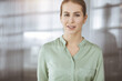 © rogerphoto - Beautiful adult business woman dressed in green blouse standing straight in sunny office. Business headshot