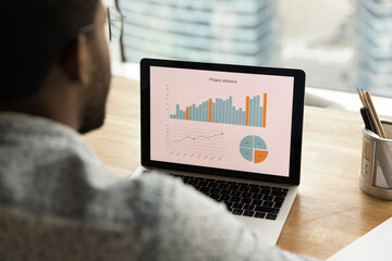 Black man sales manager financial analyst thinking on statistical information comparing data in charts graphs accessing marketing strategy effectiveness. Over shoulder view on laptop screen. Close up