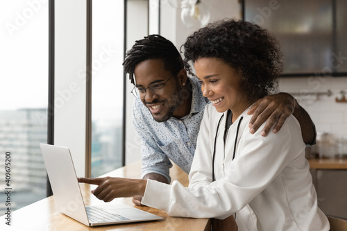 Happy smiling black couple in love cuddle at kitchen choose goods services online on laptop screen. Friendly loving african american spouses spend leisure time at home together engaged in web shopping © fizkes