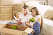 © lenetsnikolai - Portrait of happy couple looking at laptop computer together sitting in new house, surrounded with boxes