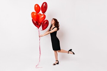 Wall Mural - Full length view of graceful girl standing on one leg with air balloons. Gorgeous ginger woman dancing on white background.