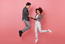 Full Length Shot Of Couple Jumping And Holding Hands. Young People Celebrating Anniversary Isolated On Pink.