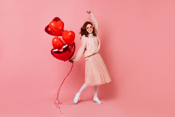 Good-looking girl with party balloons expressing sincere emotions. Studio shot of cute ginger model dancing on pink background.