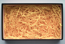 Yellow shredded crinkle paper stuffed into a cardboard box. Top view.