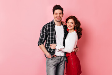 Wall Mural - Laughing ginger woman embracing husband. Studio photo of smiling couple isolated on pink.