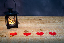 Four Red Hearts On A Wooden Background. An Illuminated Retro Lantern On The Left