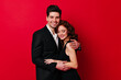 © Look! - Cute young woman hugs with husband. Studio shot of beautiful couple isolated on red.