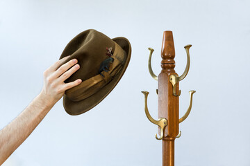 Fedora hat hanging on a wooden old fashioned antique hat rack isolated on white background. Rustic traditional vintage style head wear on coat hanger. Hand holding a fedora