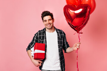 Wall Mural - Blissful guy with air balloons celebrating valentine's day. Studio shot of positive male model with present.