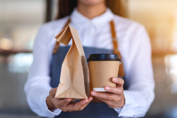 Wall Mural - Closeup of a waitress holding and serving paper cup of coffee and takeaway food in paper bag to customer in a shop