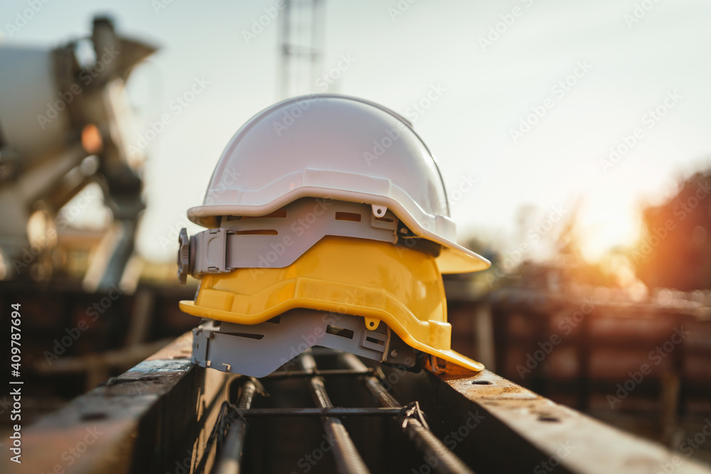 white and yellow helmet on steel in construction site - obrazy, fototapety, plakaty 
