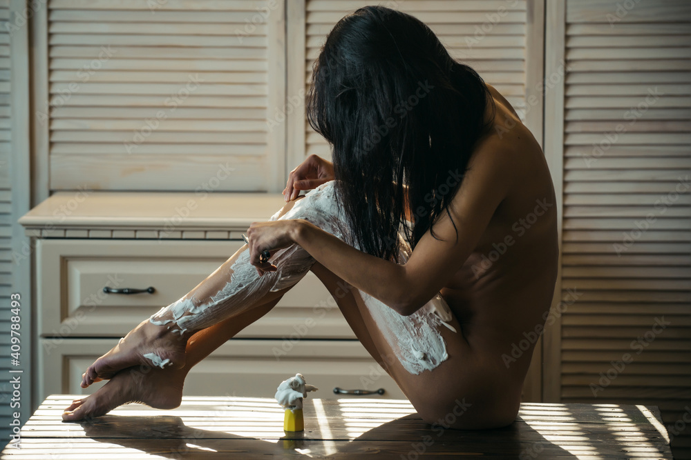 Taking care of her legs. Sexi woman removing leg hair with razor and shaving cream. Naked sexy