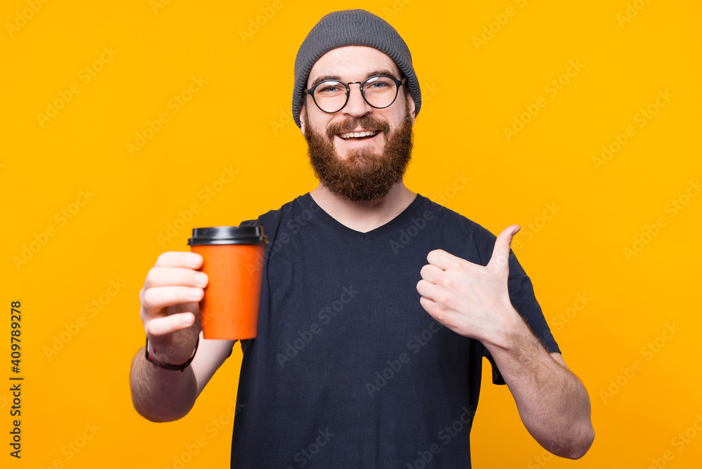 A young smilling man is enjoying his coffe and is showing a thumb up . - obrazy, fototapety, plakaty 
