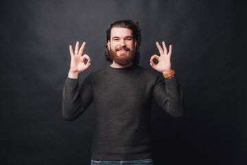 Wall Mural - A young happy and bearded man is showing the ok gesture with both hands while smiling at the camera .