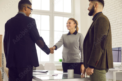 Happy young business people shaking hands to confirm collaboration after making successful deal in negotiation meeting in the office. Smiling company manager or bank adviser thanking client for trust