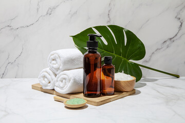 Amber glass cosmetic bottles with spa element and towel with monstera leaf on marble background. Blank label for branding mock-up. Natural beauty product concept. 