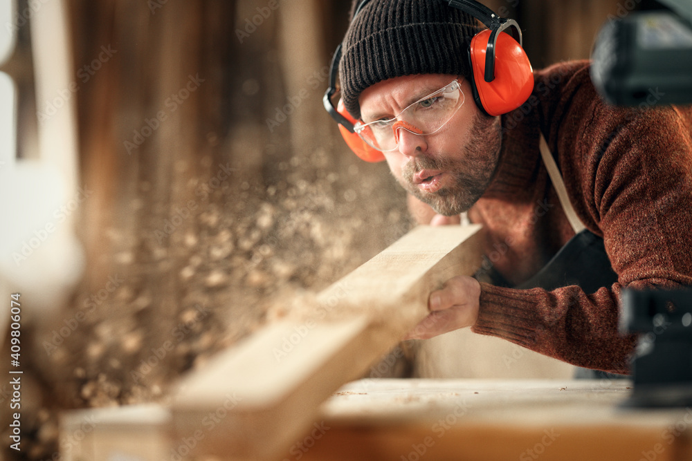 Carpenter blowing sawdust from wooden plank - obrazy, fototapety, plakaty 