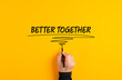 Male hand writing the message better together on yellow background. Corporate teamwork, solidarity and cooperation