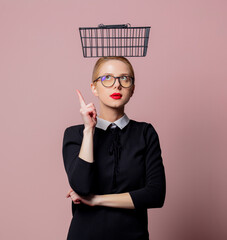 Wall Mural - Blonde woman black dress and glasses with shopping basket on pink background